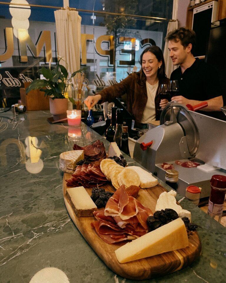 Couple with glasses of red wine at the bar, a cheese and charcuterie board in front of them