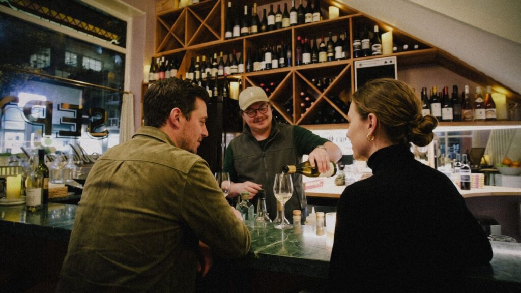 Ed Rava pouring white wine for two guests at the green marble bar