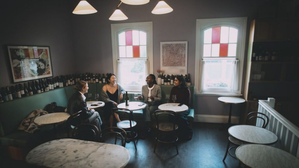 Four guests talking on the green banquette upstairs, under stained-glass windows
