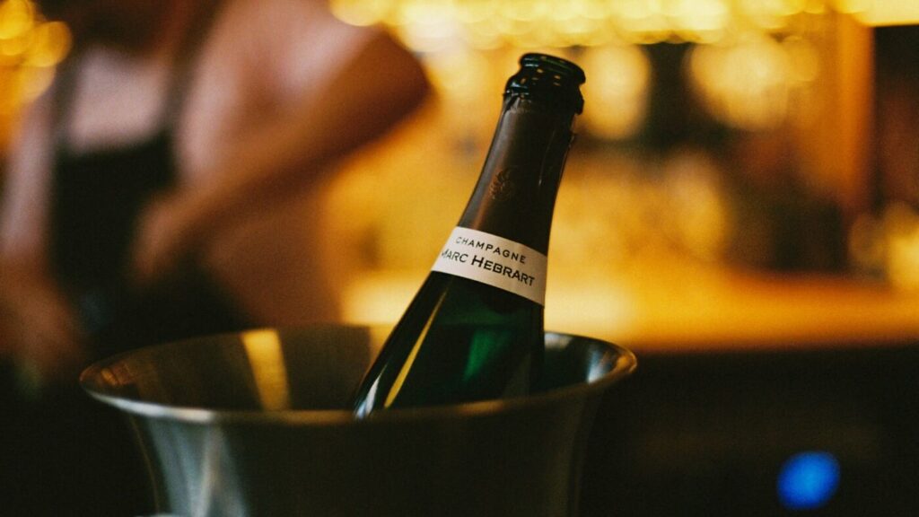 A bottle of Champagne chilling in a silver ice bucket on the bar at Bar Septimus, warm lights behind