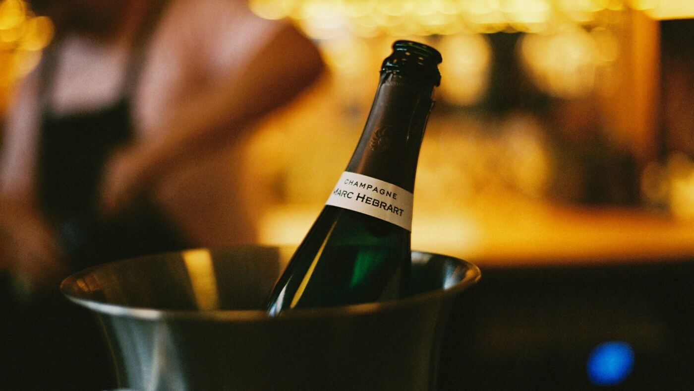 A bottle of Champagne chilling in a silver ice bucket on the bar at Bar Septimus, warm lights behind