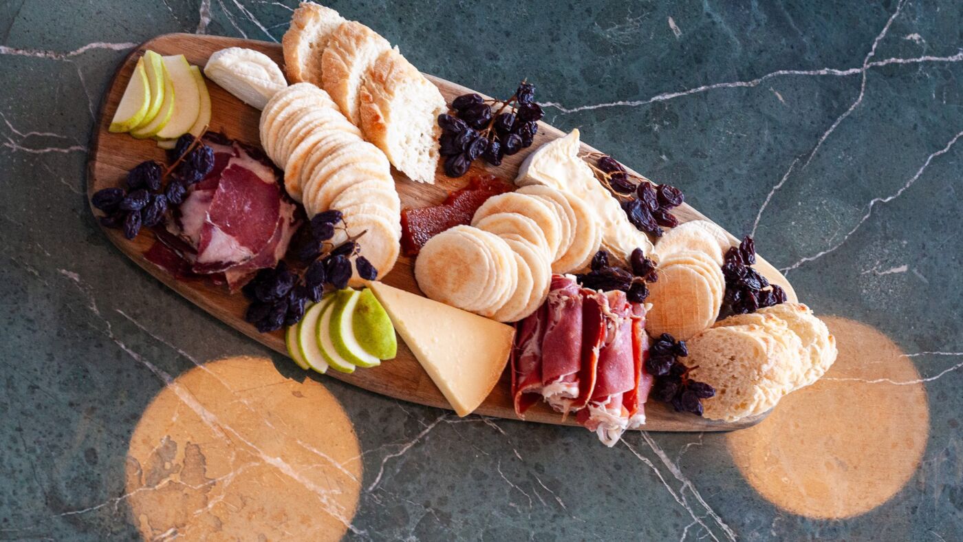 Overhead view of a cheese and charcuterie board with crackers, pear and muscatels on green marble at Bar Septimus