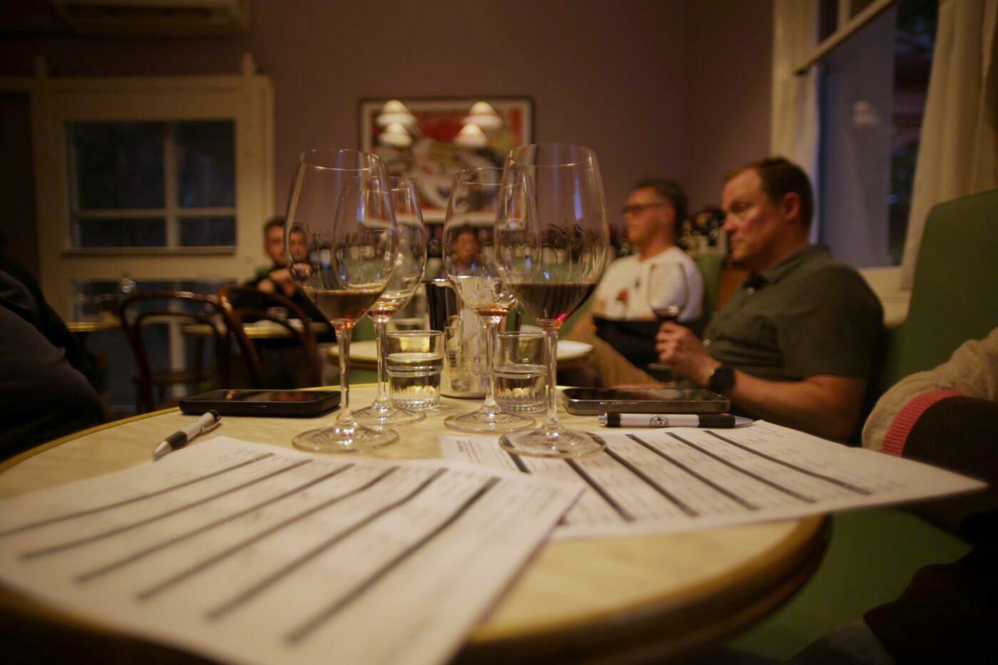 Players mid-round, glasses lined up beside handwritten answer sheets
