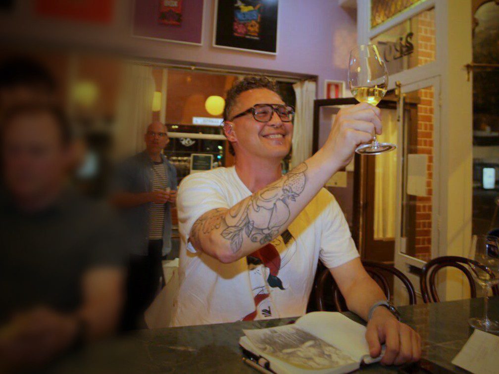 A guest at the counter raising a glass of white wine to the light