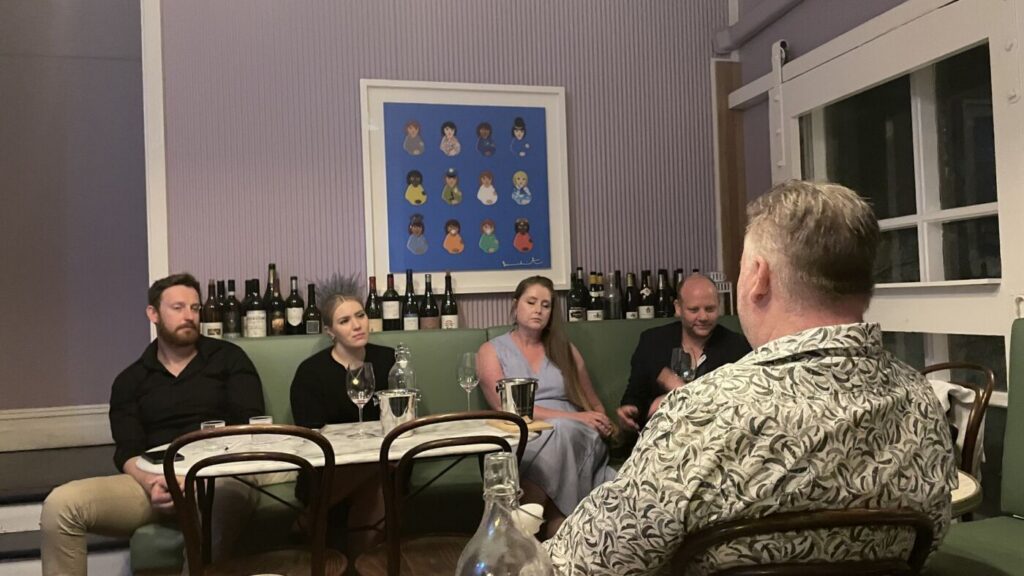 A host talking guests through a tasting on the green banquette upstairs at Bar Septimus, bottles lined up behind