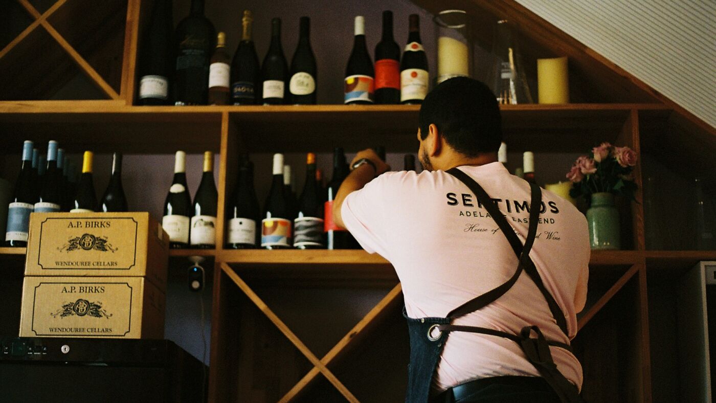 A Bar Septimus team member reaching for a bottle from the timber wine shelves, wooden wine cases below